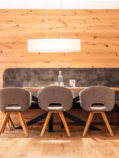 Ein modernes Esszimmer mit einem Holzpaneel-Hintergrund. Ein großer Tisch, umgeben von beigen Stühlen und einer stilvollen Deckenlampe.