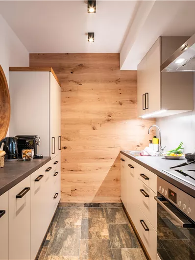 Eine moderne Küche mit warmen Holzdetails und einem klaren, funktionalen Design. Auf der Arbeitsplatte stehen frisches Obst und Küchengeräte.