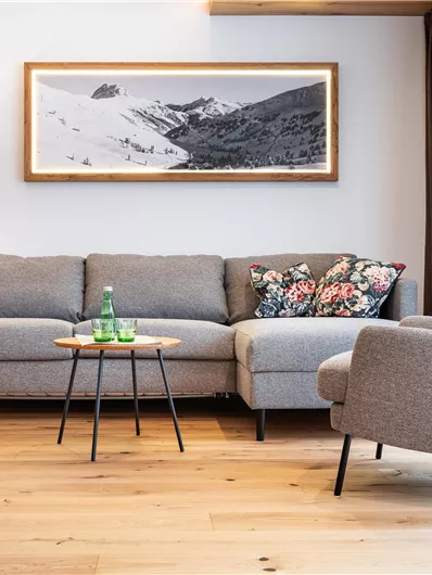 Ein modernes Wohnzimmer mit einem grauen Sofa und einem bequemen Sessel. Ein Holztisch und eine Stehlampe sorgen für eine gemütliche Atmosphäre.