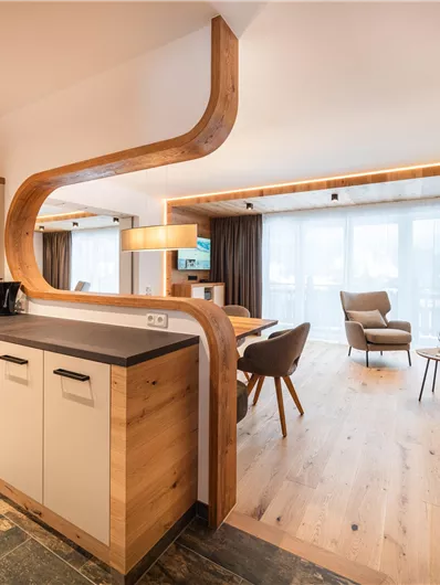 Eine moderne Wohnküche mit Holzdetails und offenem Wohnbereich. Große Fenster lassen viel Licht herein und schaffen eine gemütliche Atmosphäre.