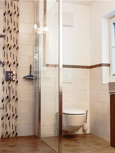 A modern bathroom with a walk-in shower and a toilet. The walls are brightly tiled, and there are wooden details that create a cozy atmosphere.