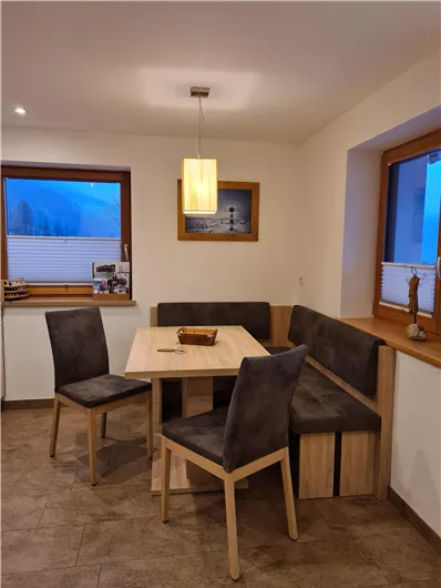 A cozy dining area with a wooden table and upholstered chairs. The large windows offer a view outside and let in plenty of light.