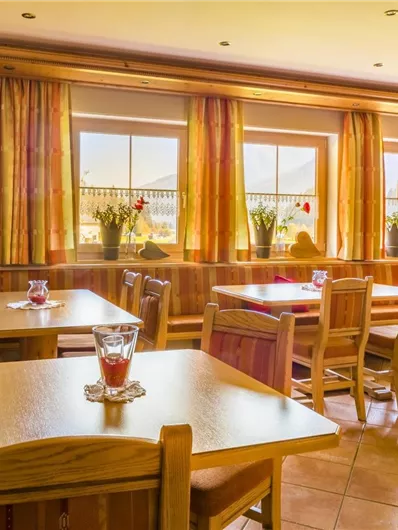 Een gezellig restaurant met houten meubels en grote ramen. De tafels zijn netjes gedekt en er zijn planten en bloemen in de ruimte.