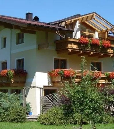 A beautiful house with flower balconies and a clear blue sky. Surrounded by green grass and trees.