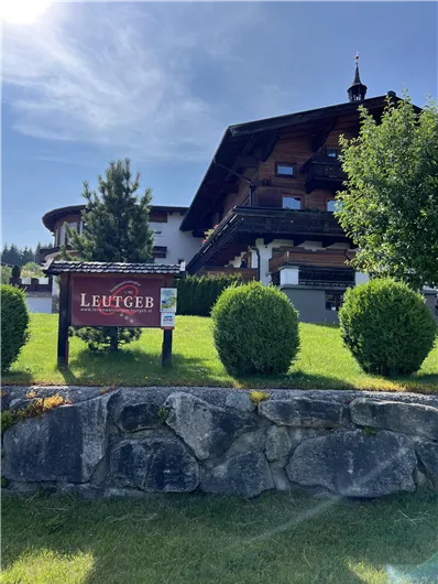 A traditional Tyrolean chalet surrounded by well-kept greenery. In the foreground, there is a sign with the inscription "Leutgeb".