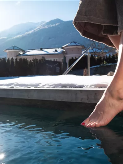 A foot standing at the edge of a swimming pool, with mountains in the background. The sun is shining and it is a clear, beautiful day.