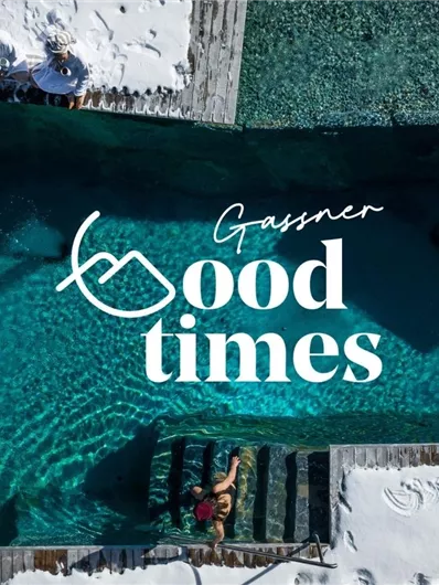A beautiful pool with clear blue water and surrounded by snow. Above it is the inscription "Gassner Good Times".