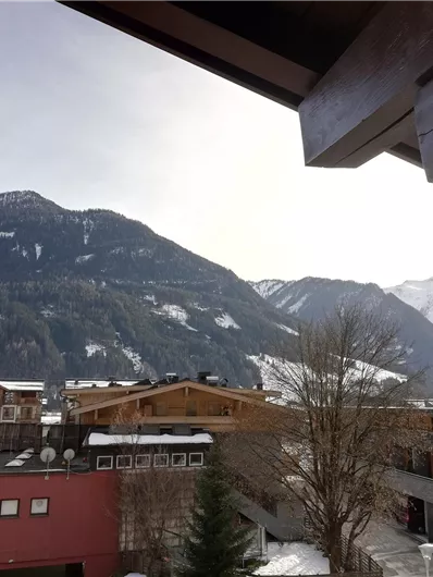 Een schilderachtig berglandschap met sneeuwbedekte toppen. Op de voorgrond zijn moderne gebouwen en bomen te zien.