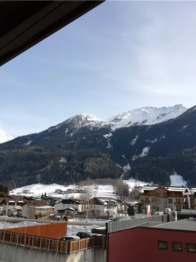 Een winterlandschap met besneeuwde bergen en een rustig dorp in de vallei. De lucht is helder en zonnig.