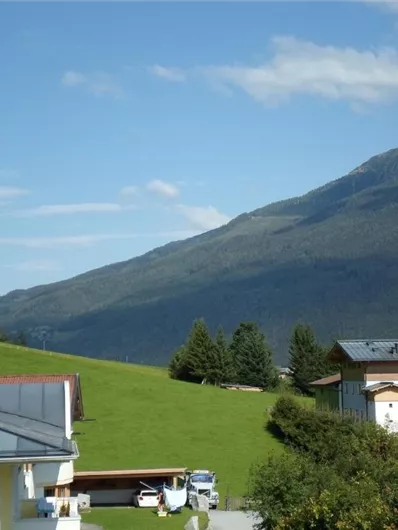 Een schilderachtig Alpenlandschap met groene heuvels en majestueuze bergen. Op de voorgrond zijn enkele gezellige huizen te zien.