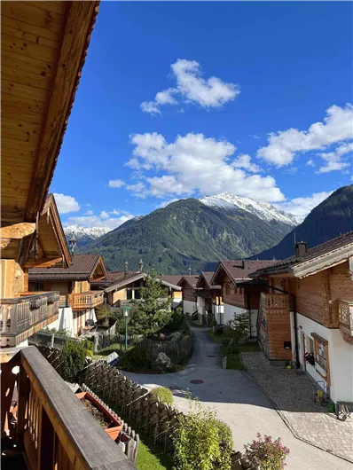 Eine malerische Berglandschaft mit traditionellen Chalets und schneebedeckten Gipfeln. Der Himmel ist klar und blau, ideal für einen entspannten Aufenthalt in den Alpen.