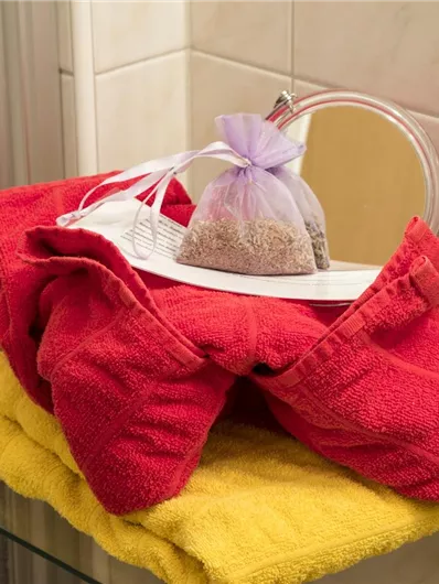 Een stapel kleurrijke handdoeken in een badkamer. Bovenop ligt een zak met een kleine inhoud.