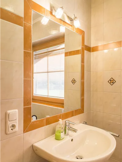 Een moderne badkamer met een wastafel en een grote spiegel. Het ontwerp is licht en vriendelijk, met tegels in zachte kleuren.