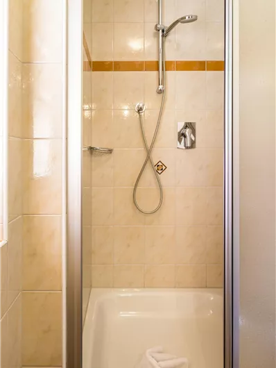 Een kleine douchecabine met tegels in lichte kleuren. De douche is uitgerust met een handdouchekop en een handdoek.