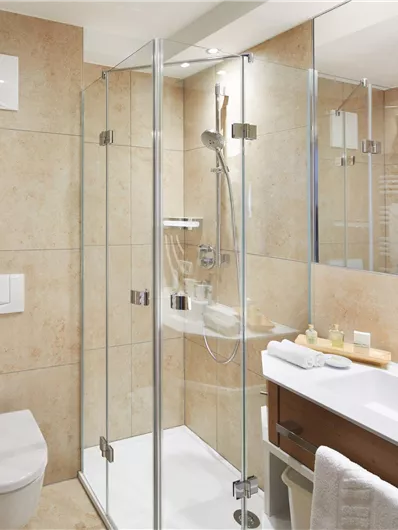 Ein modernes Badezimmer mit einer klaren Duschabtrennung aus Glas. Die Wände sind mit beigem Fliesen und die Ausstattung ist praktisch und elegant.