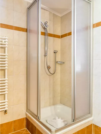 Een moderne douchecabine in een heldere badkamer. De muren zijn betegeld en een handdoekhouder is zichtbaar.