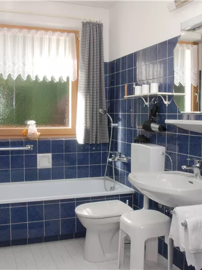 Ein modernes Badezimmer mit blauen Fliesen. Es enthält eine Badewanne, ein Waschbecken und eine Toilette.