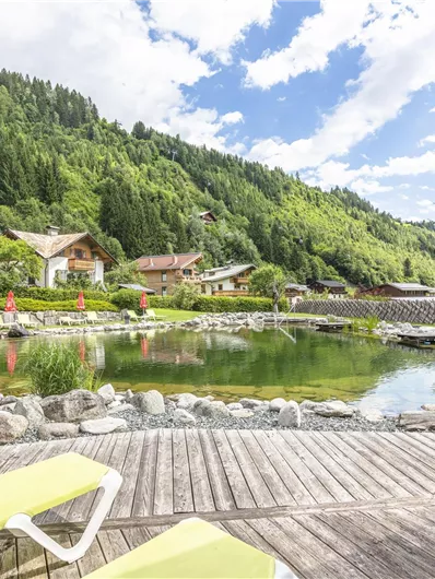 A beautiful natural lake surrounded by green hills and alpine cabins. Sun loungers invite you to relax.
