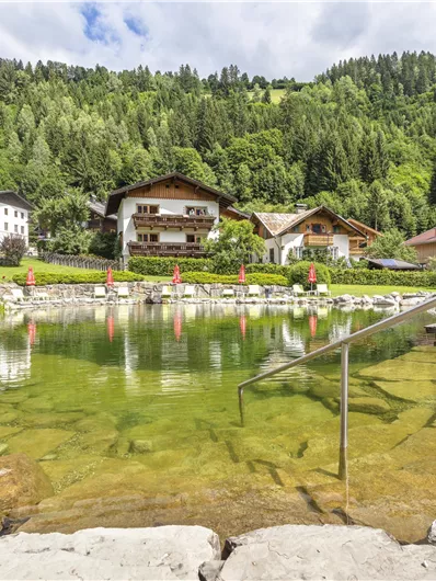 A green natural pond surrounded by mountains and traditional houses. The atmosphere feels calm and inviting.