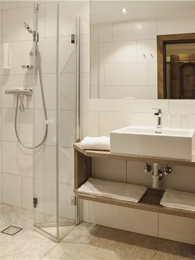 Ein modernes Badezimmer mit zwei Duschkabinen und einem Waschbecken auf einer Holzablage. Die Wände sind in hellem Weiß gefliest, was einen sauberen und eleganten Look vermittelt.