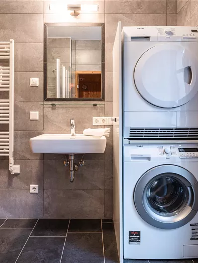 Ein modernes Badezimmer mit einer Waschmaschine und einem Trockner. Es gibt ein Waschbecken und eine große Dusche.