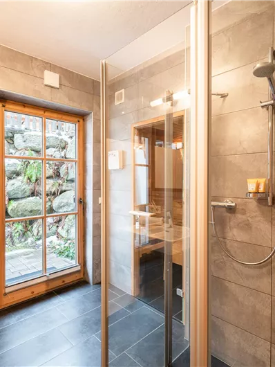 Ein modernes Badezimmer mit Glasduschabtrennung und einem großen Fenster. Natürliche Materialien und viel Licht schaffen eine einladende Atmosphäre.