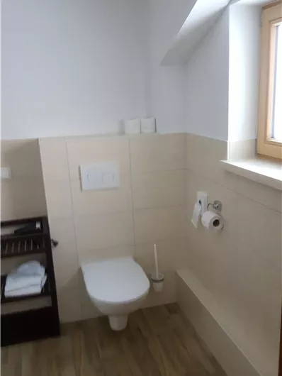 Ein modernes Badezimmer mit einer Toilette und einem Fenster. Es gibt auch einen Regal mit Handtüchern und Toilettenpapier.