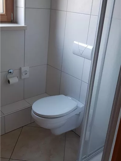 Ein kleines Badezimmer mit einer Dusche und einer Toilette. Die Wände sind gefliest und es gibt ein Fenster für natürliches Licht.