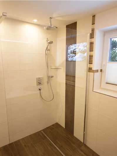 A modern bathroom with a large shower and a window. The walls are brightly tiled and the floor is made of wood.