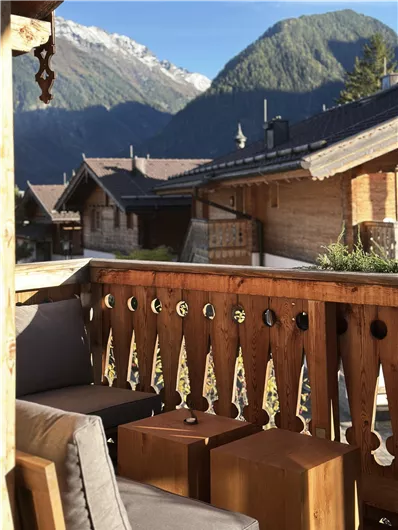 Ein gemütlicher Balkon mit Holzgeländer und Sitzgelegenheiten bietet einen Blick auf die Berge. Die Umgebung ist ruhig und idyllisch, umgeben von traditionellen Chalets.