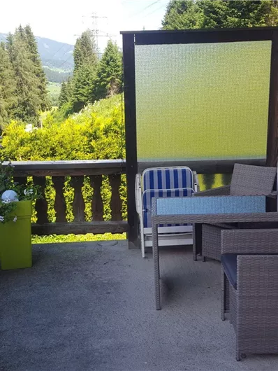 Ein gemütlicher Balkon mit Gartenmöbeln und Blick auf grüne Bäume und Berge. Der Bereich ist hell und einladend.