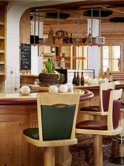 Een gezellige bar met houten planken en een ronde toog. De stoelen zijn in hout- en groentinten gehouden en er zijn decoratieve planten.
