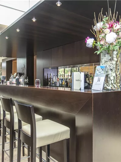 A modern bar with dark wood interiors and elegant chairs. Decorative flowers and drinks are on the counter in a stylish setting.