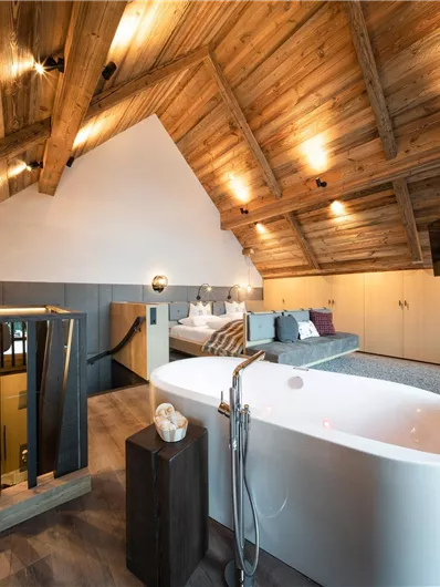 Ein modernes Zimmer mit Holzdecken und einer freistehenden Badewanne. Gemütliche Einrichtung und viel Licht schaffen eine einladende Atmosphäre.