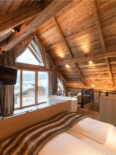 Ein gemütliches Zimmer im Dachgeschoss mit Holzdecken und warmem Licht. Große Fenster bieten einen schönen Ausblick auf die Umgebung.