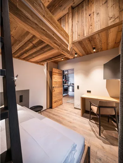 Ein modernes Zimmer mit Holzdecke und rustikalem Design. Es gibt ein Bett, einen Schreibtisch und einen Zugang zu einem holzverkleideten Platz.
