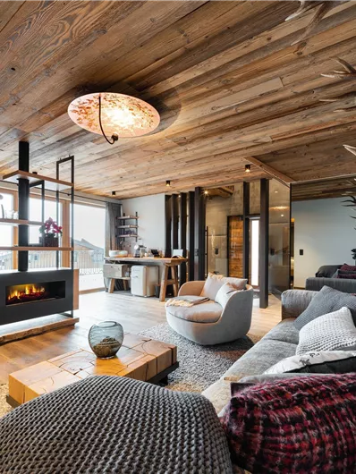 Ein modernes Wohnzimmer mit Holzdecken und einem stilvollen Kamin. Gemütliche Möbel und ein einladendes Ambiente schaffen eine entspannte Atmosphäre.