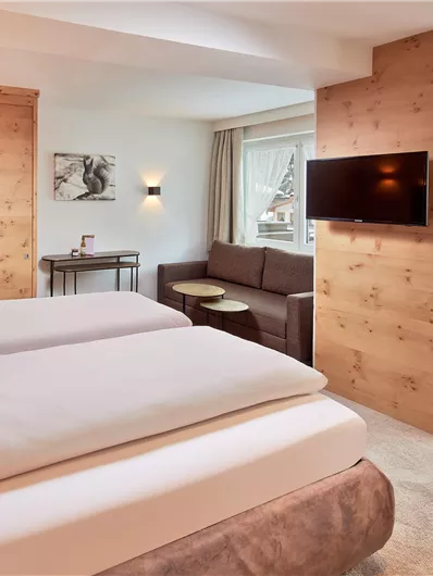Ein gemütliches Zimmer mit zwei Betten und Holzverkleidung. Es enthält einen Sitzbereich und einen Tisch, mit Fenstern, die viel Licht hereinlassen.