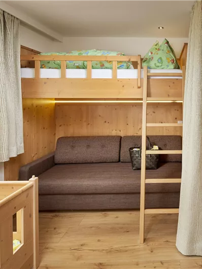 Ein gemütliches Zimmer mit einem Hochbett und einer Schlafcouch. Der Raum hat helle Vorhänge und warmen Holzfußboden.