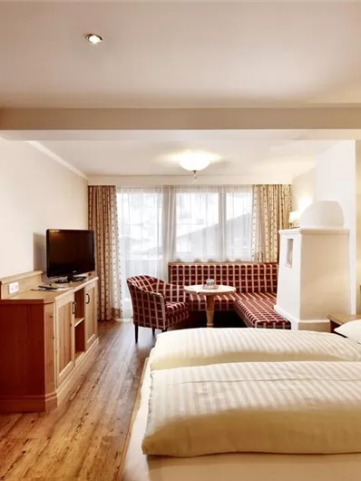 Een gezellige hotelkamer met twee bedden, houten vloeren en een televisie. Er is een zithoek met een tafel en ramen met uitzicht op de natuur.