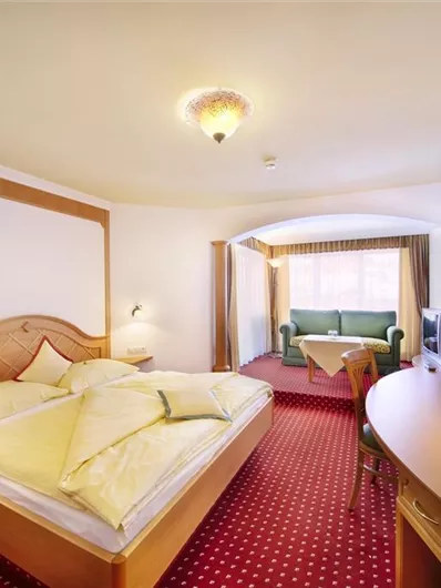 Een gezellig hotelkamer met een groot bed en een tafel. Er is een zithoek met een groene bank en veel daglicht.