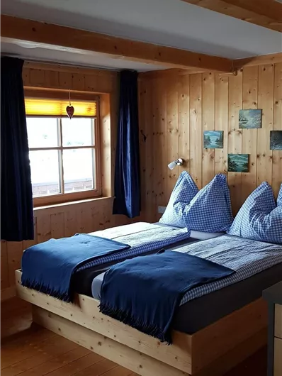Ein gemütliches Schlafzimmer mit Holzvertäfelungen. Zwei Betten mit blauen Decken und Kissen, und ein Fenster, das natürlichen Licht hereinlässt.