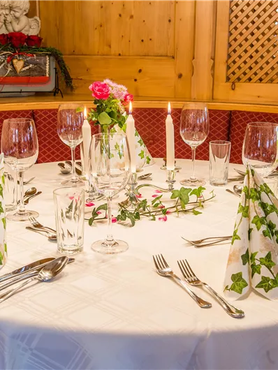 Ein festlich gedeckter Tisch mit weißen Stoffservietten und Gläsern. Einige Blumen und Kerzen sorgen für eine einladende Atmosphäre.