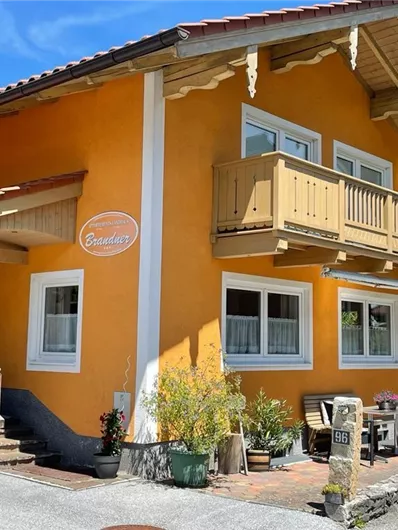 A charming orange house with a balcony.  
Surrounded by plants and a green landscape background.
