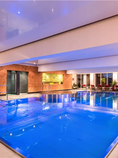 Ein modernes Hallenbad mit klarem, blauem Wasser. Die Umgebung ist elegant gestaltet, mit gemütlichen Liegen und sanfter Beleuchtung.