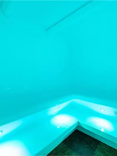 Ein modernen, hellblau beleuchtetes Badezimmer mit einer Dusche. Die Wände und die Badewanne sind in einem minimalistischen Design gehalten.