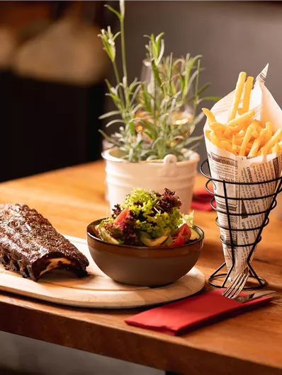 A delicious plate of ribs, fresh salad, and crispy fries. Accompanied by a glass of red wine on an elegant table.