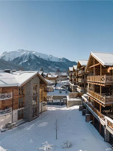 A picturesque mountain village in the snow with modern chalets. The surroundings are surrounded by impressive mountains and a clear blue sky.