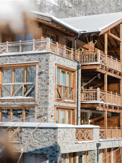 A modern wooden mountain cabin in a snowy landscape. The buildings have large windows and balconies with a view of nature.