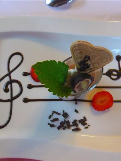 Een kunstzinnig gepresenteerd dessert op een wit bord. Het toont een muzikale noot van chocolade, een hartvormig wafelstuk en verse aardbeien.
